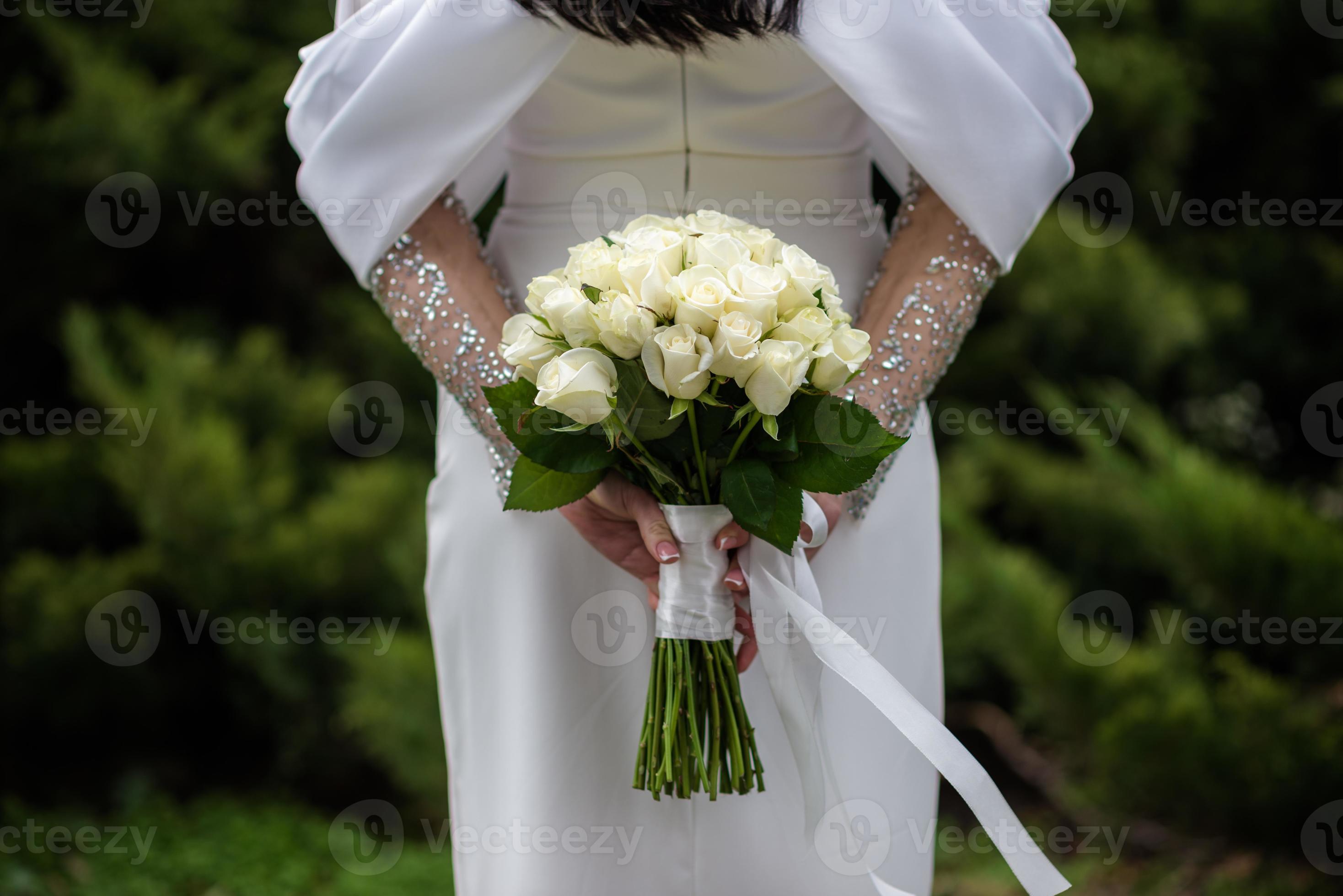 a noiva em um vestido de noiva branco está segurando um buquê de flores  brancas - peônias, rosas. Casamento. noiva e noivo. delicado buquê de  boas-vindas. bela decoração de casamentos com folhas
