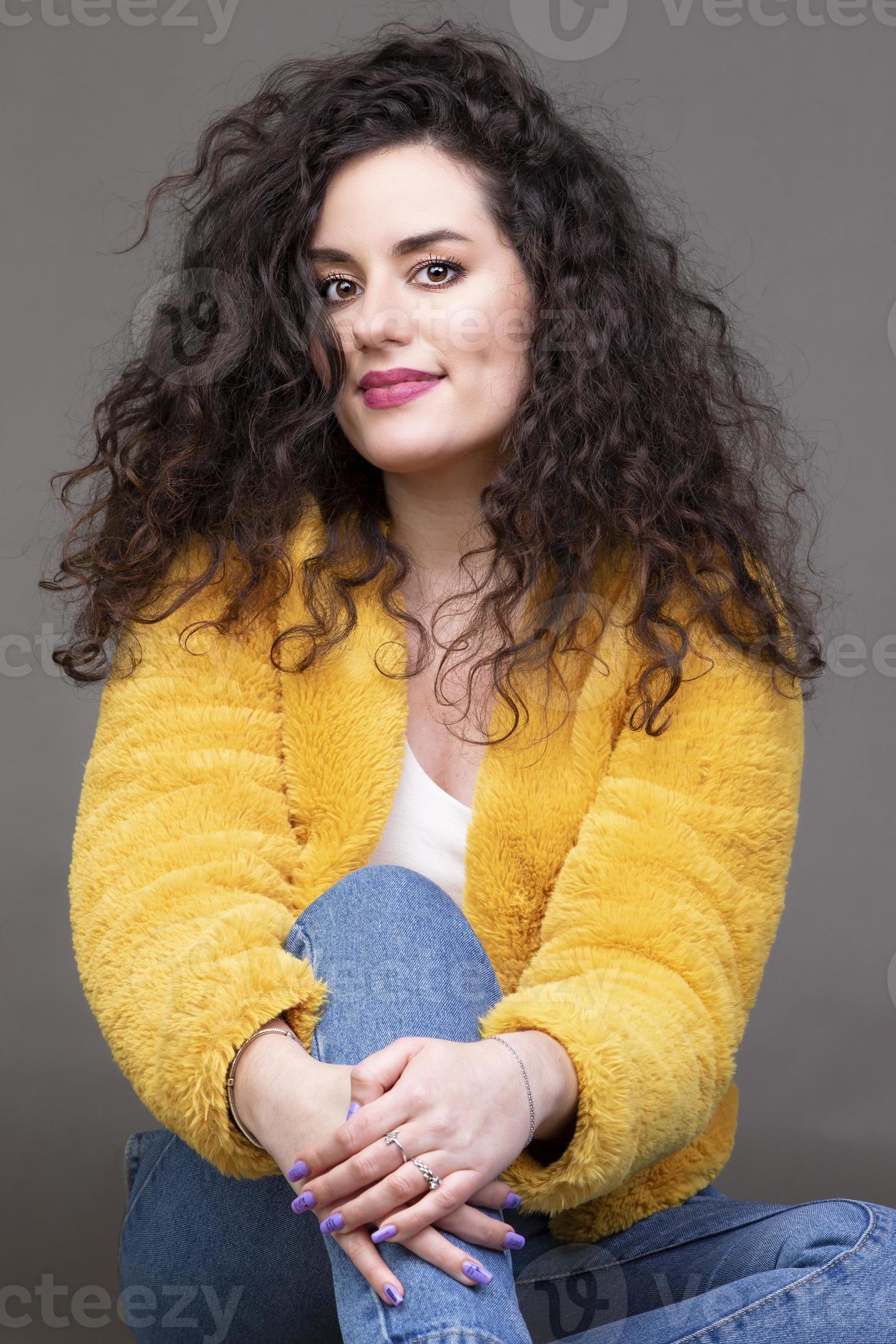 uma linda menina morena com cabelos cacheados em um casaco de pele amarelo  olha para a câmera e sorri. uma garota com aparência espanhola. 19089388  Foto de stock no Vecteezy