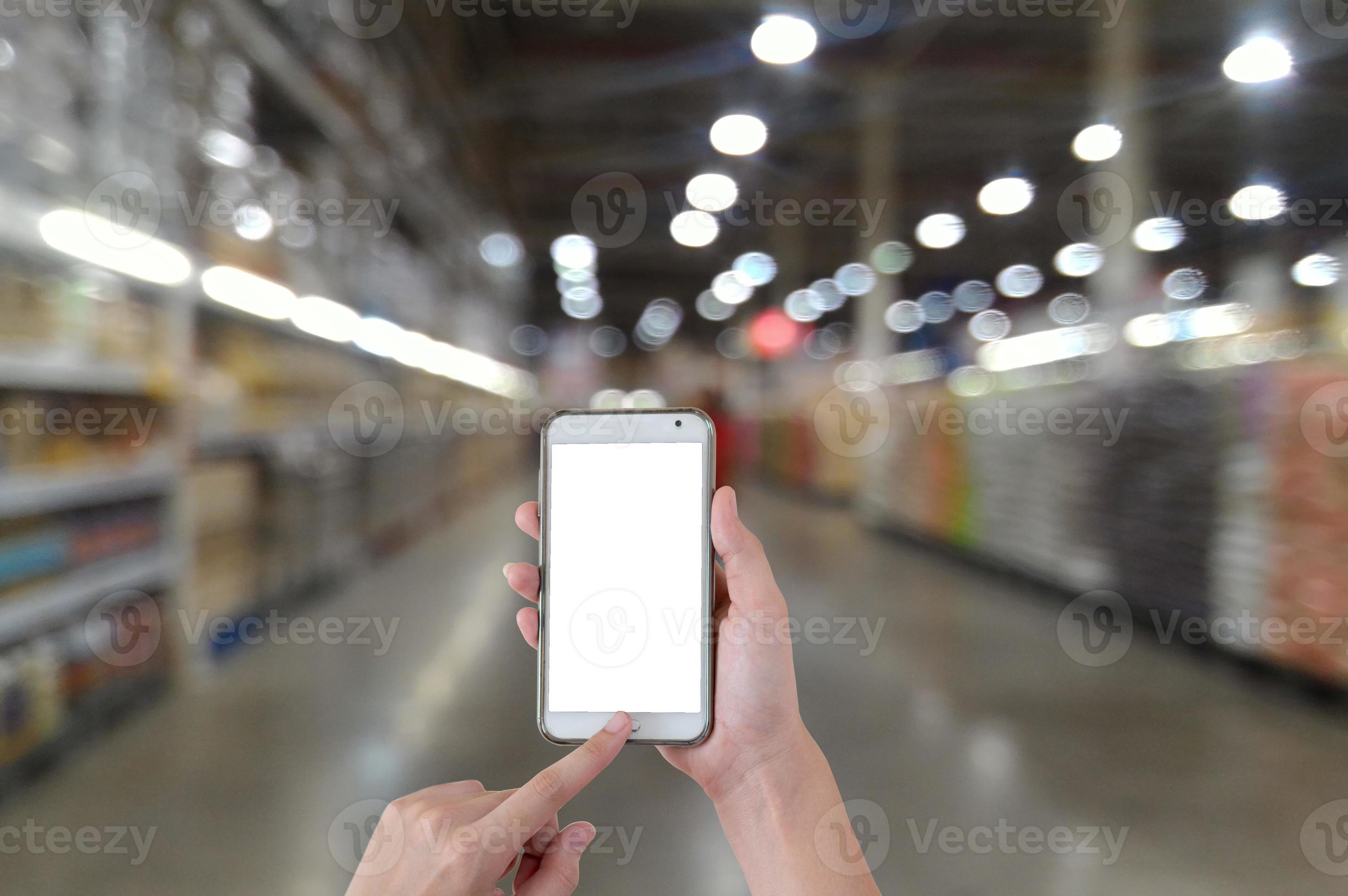mãos usando um telefone móvel inteligente de tela em branco com fundo desfocado no supermercado foto