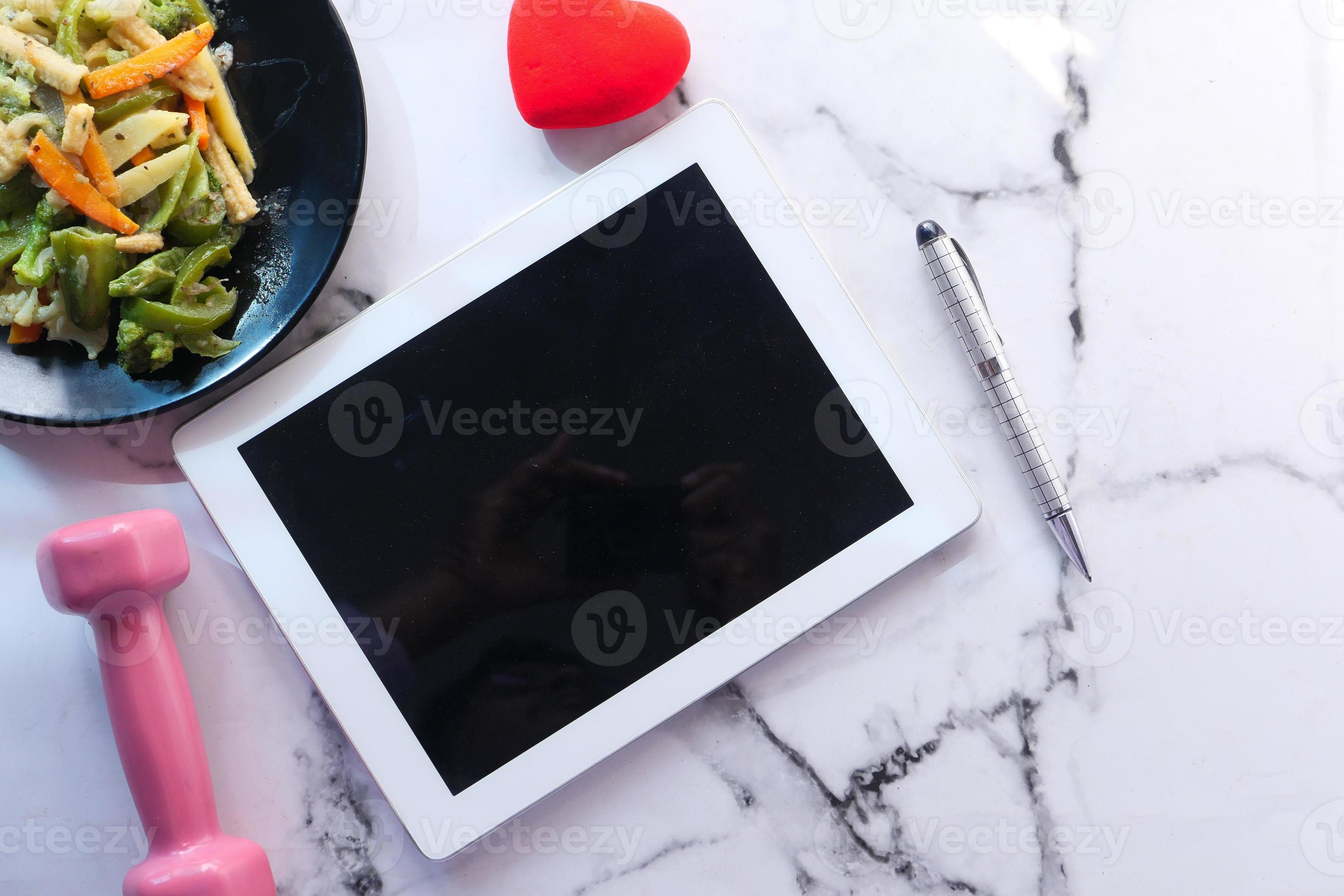 tablet digital em bancada de mármore com halteres e salada foto