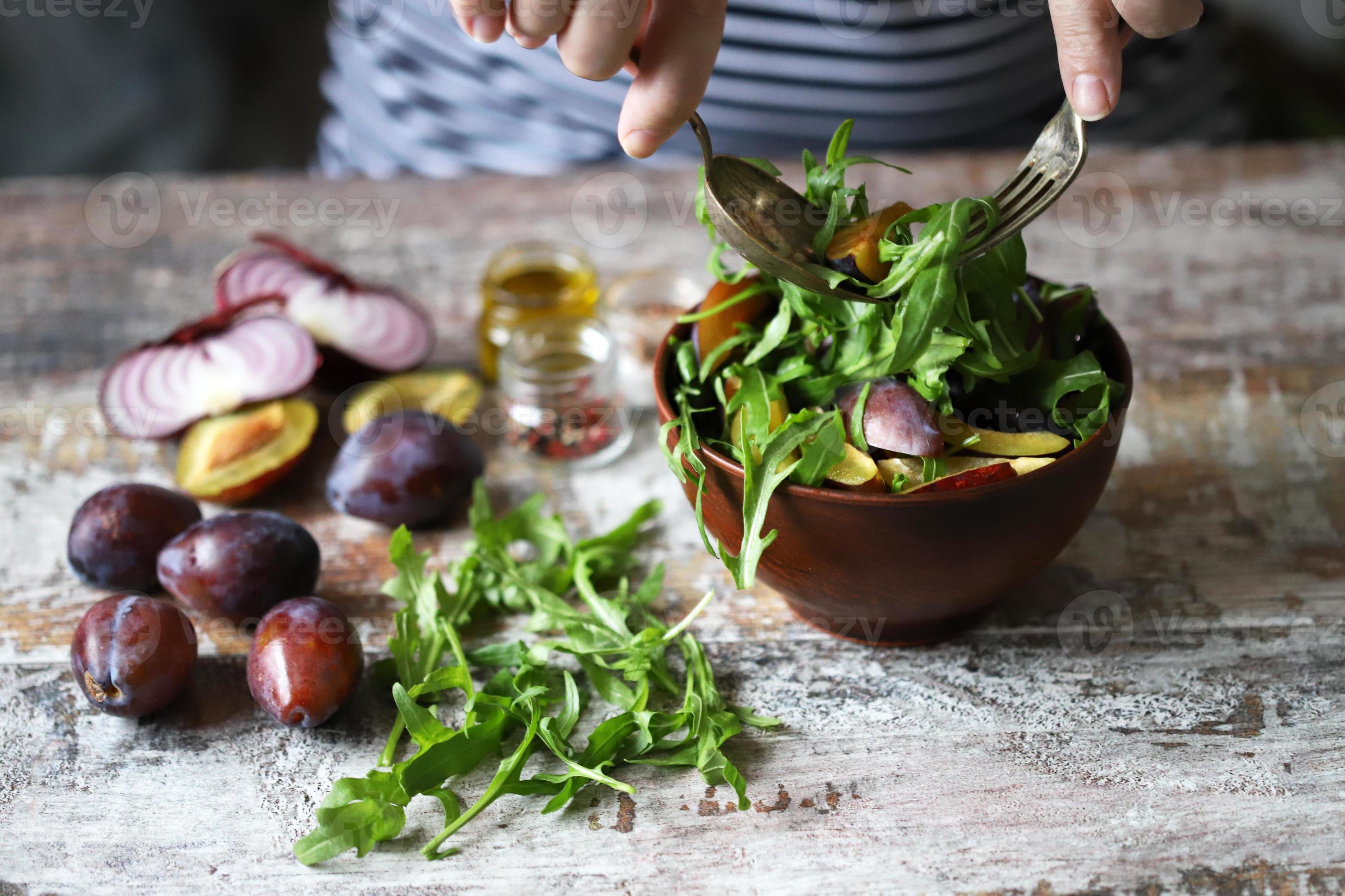 salada saudável misture as mãos masculinas com uma colher e um garfo. salada de ameixa de rúcula. foto