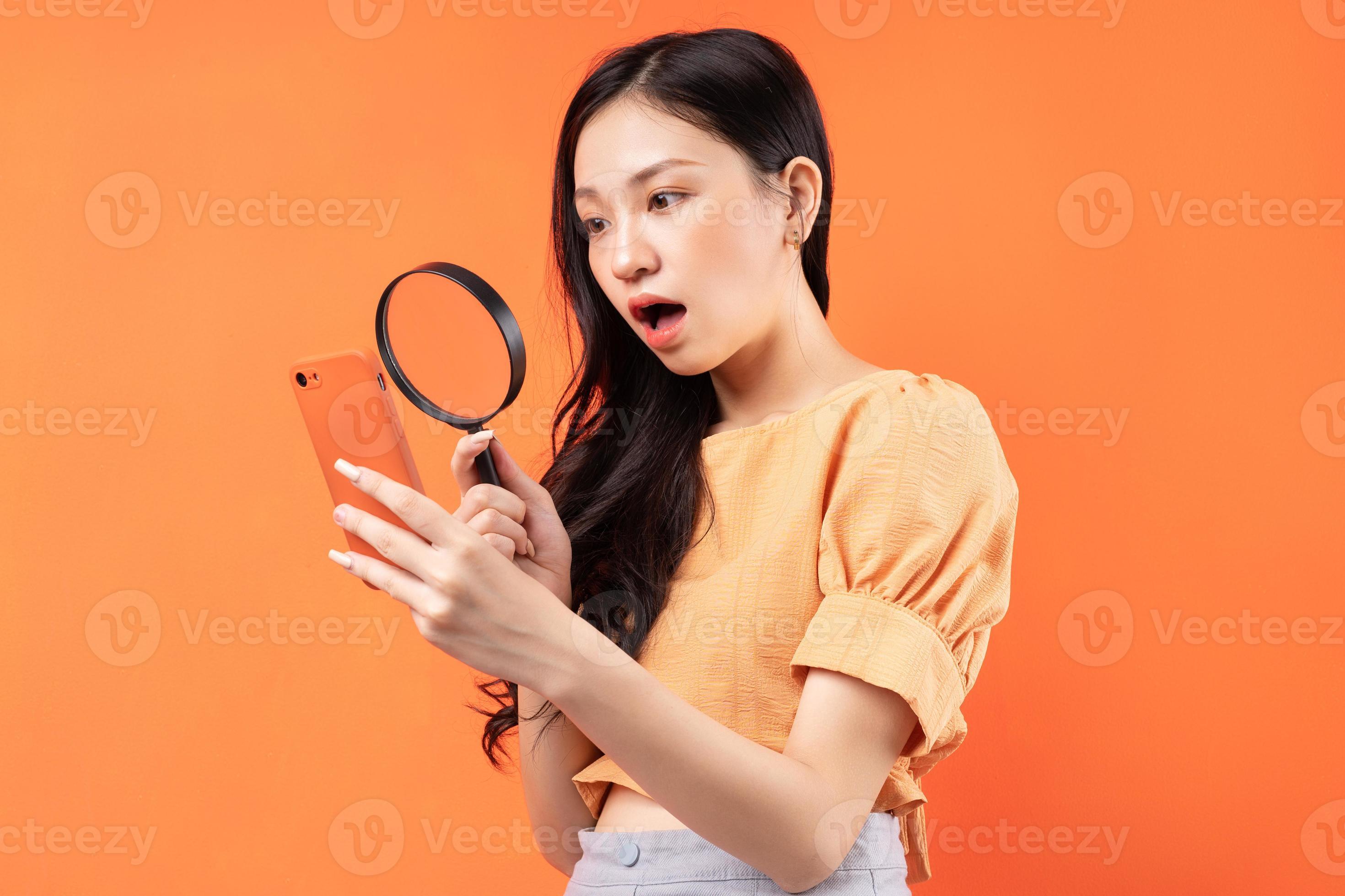 mulher segurando uma lupa olhando para o telefone com uma expressão de surpresa foto