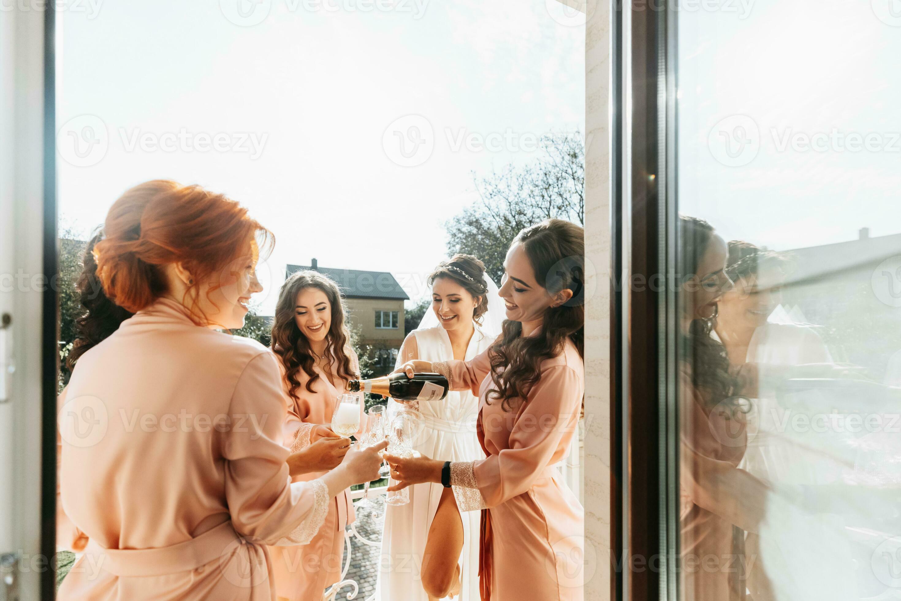 jovem damas de honra estão tendo Diversão e sorridente dentro Rosa seda  vestes bebendo champanhe às a da noiva gazebo. lindo mulheres comemoro uma  solteira festa, dentro uma gazebo e com champanhe.