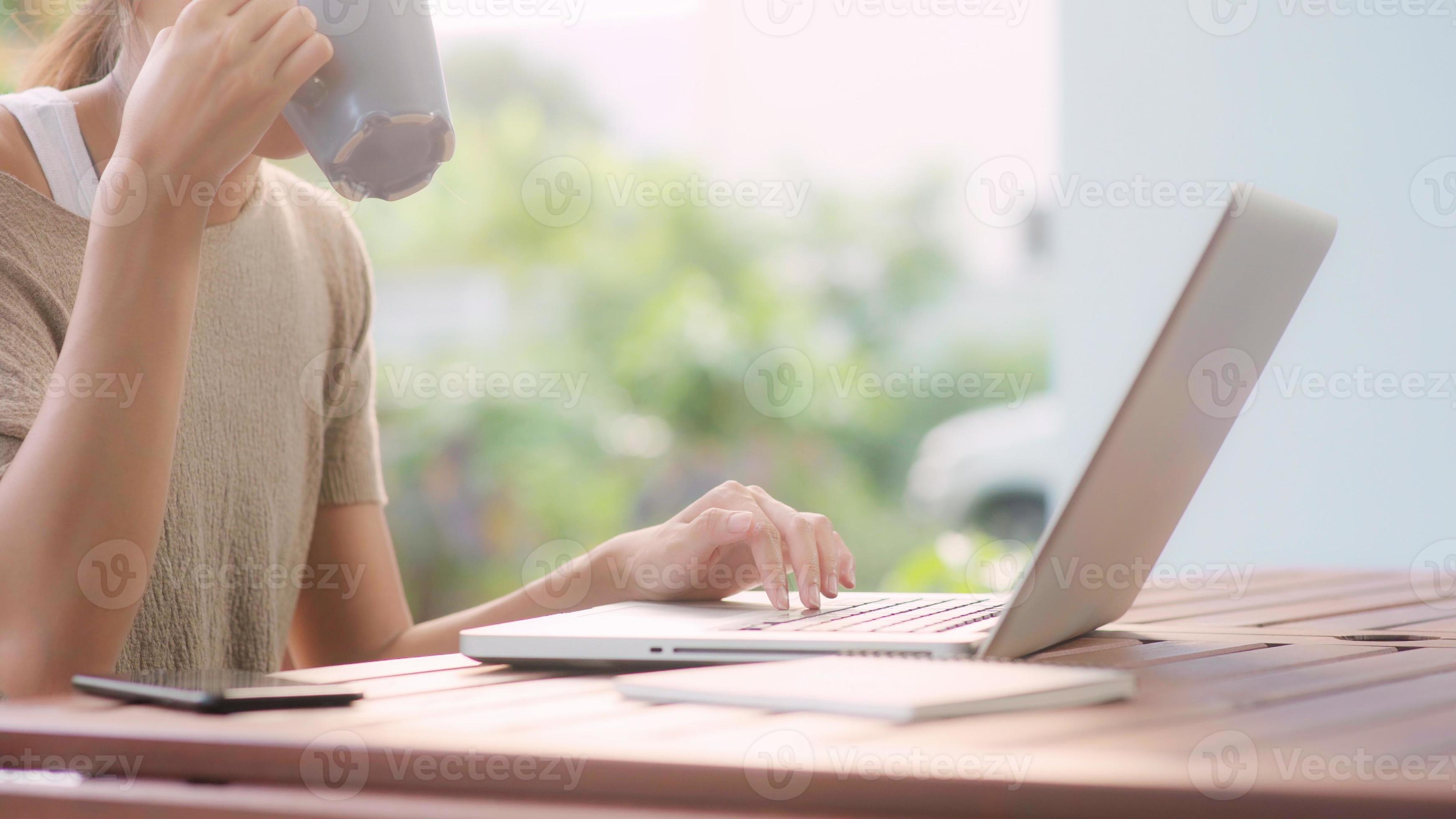 mulher asiática freelance trabalhando em casa, mulher de negócios trabalhando no laptop e bebendo café sentado na mesa no jardim pela manhã. mulheres de estilo de vida trabalhando no conceito de casa. foto