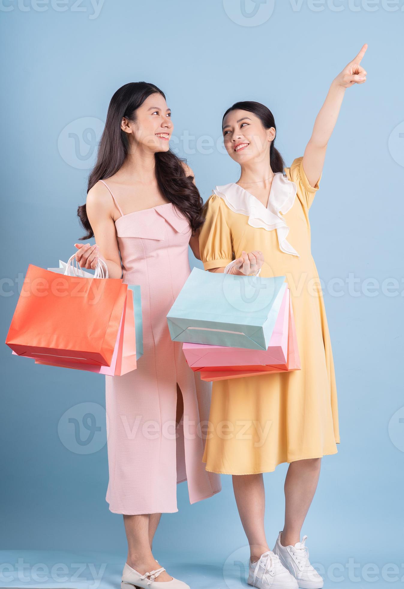 duas jovens mulheres asiáticas segurando uma sacola de compras sobre fundo azul foto