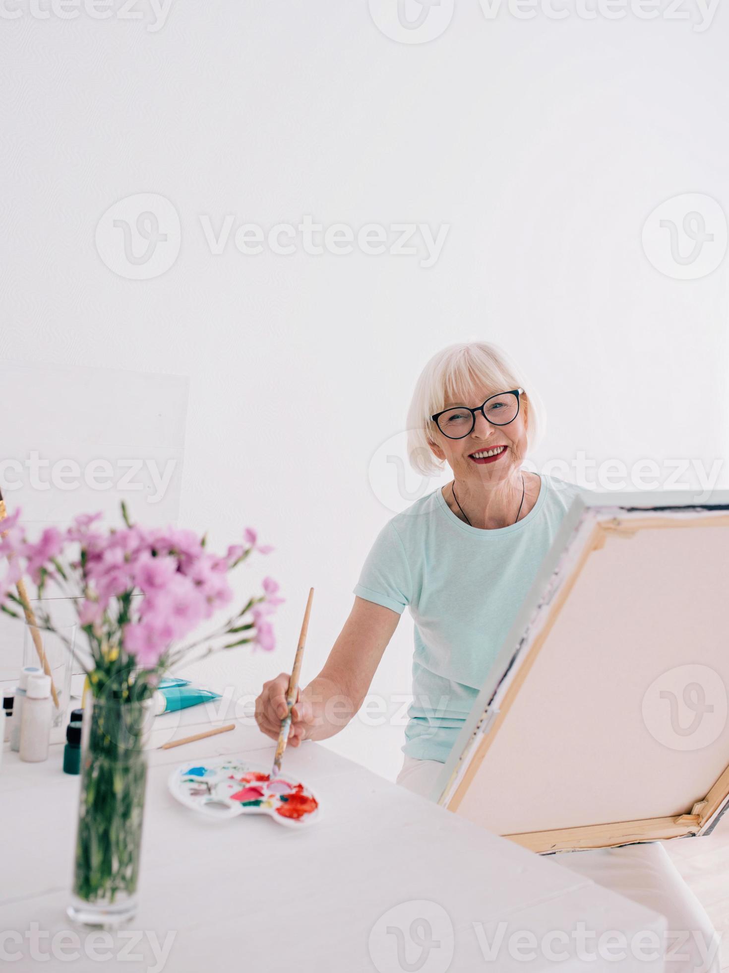 artista sênior de mulher alegre em copos com cabelos grisalhos, pintura de flores em um vaso. criatividade, arte, hobby, conceito de ocupação foto
