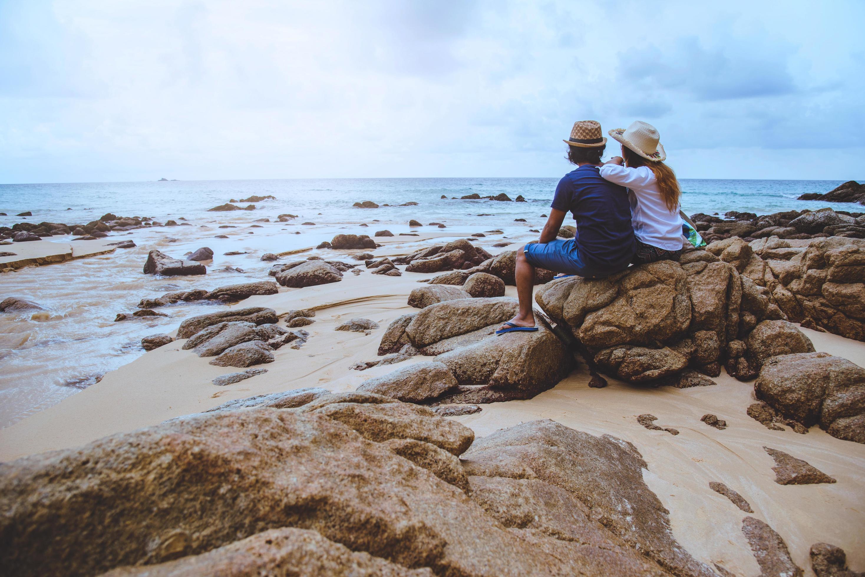 amantes asiáticos felizes na praia. o céu é a natureza de viagens brilhantes e sentar-se relaxar nas rochas no mar em phuket. Na Tailândia. verão. foto