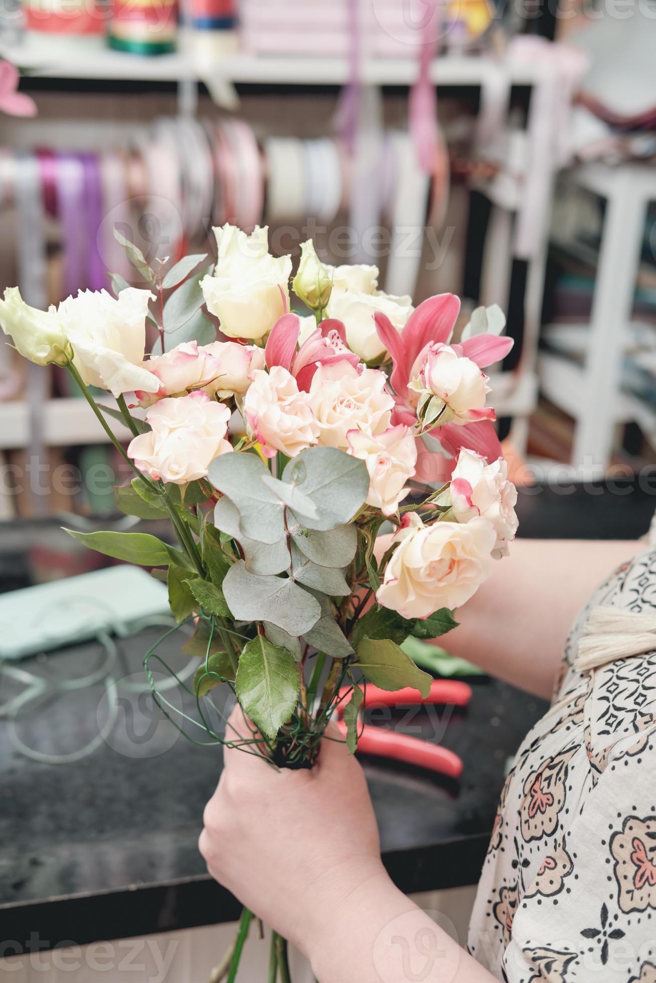 florista de mulher fazendo buquê de casamento delicado para uma noiva.  folhas de eucalipto, pequenas rosas e orquídeas nas mãos do florista.  5448746 Foto de stock no Vecteezy