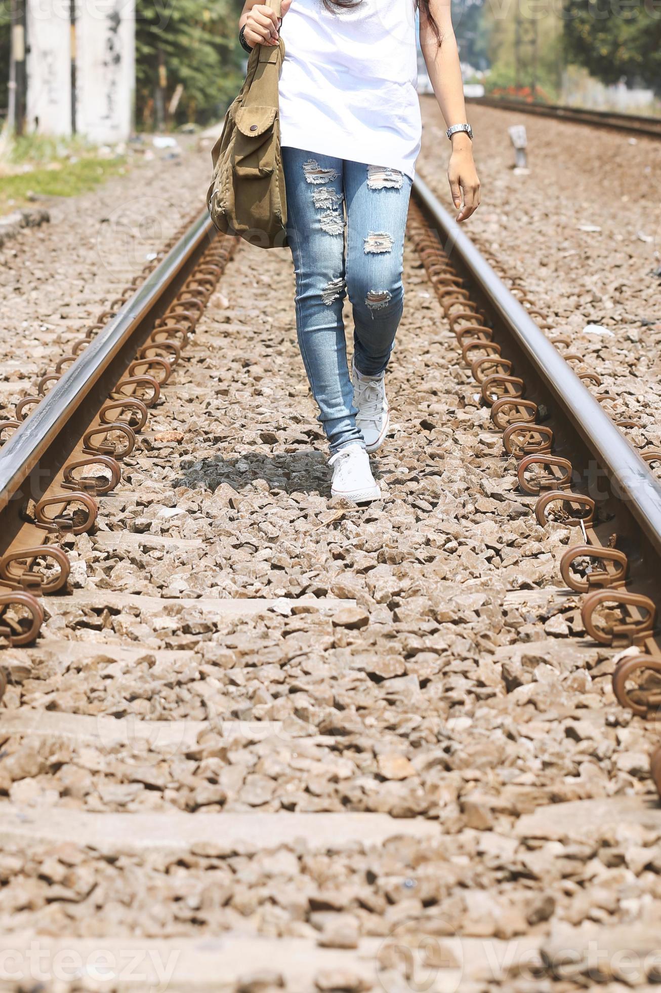 menina andando na ferrovia vestindo jeans rasgados, saco de sling
