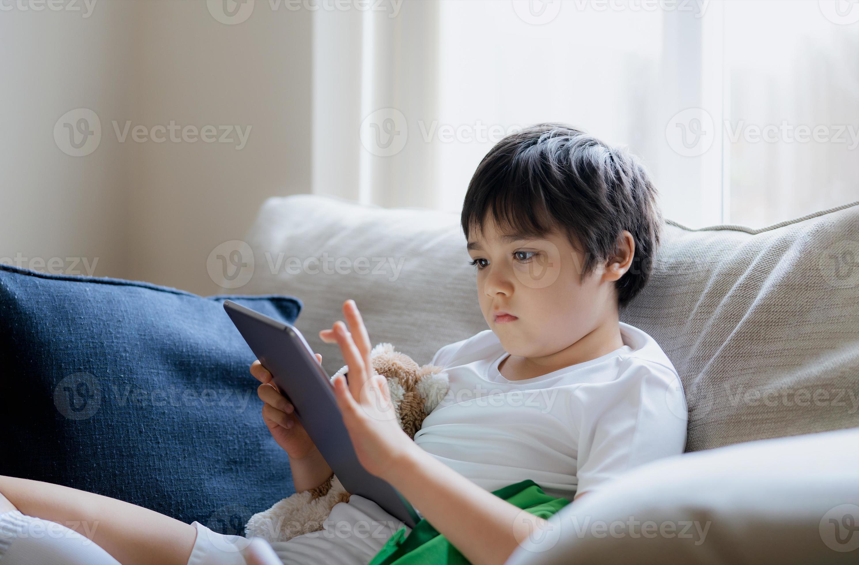 criança jogando jogos online na internet no quarto, retrato de menino  usando tablet digitando ou conversando com amigos de manhã, infância  sentada na cama fazendo lição de casa, criança da escola com