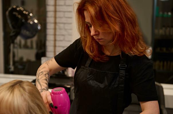 Cabeleireiro seca e modela o cabelo com um secador de cabelo no salão de  beleza