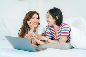 lgbtq, conceito lgbt, homossexualidade, retrato de duas mulheres asiáticas posando felizes juntos e se amando enquanto jogava computador laptop na cama foto