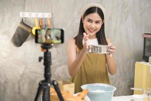 linda mulher está fazendo padaria enquanto transmite ao vivo ou grava vídeo nas mídias sociais em sua casa, conceito de negócio de cafeteria. foto