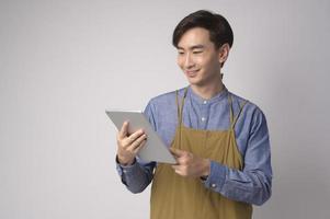 retrato de jovem asiático vestindo avental segurando tablet sobre estúdio de fundo branco, conceito de empresário foto