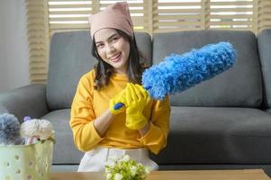 jovem mulher feliz usando luvas amarelas e segurando uma cesta de material de limpeza na sala de estar. foto