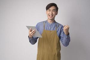 retrato de jovem asiático vestindo avental segurando tablet sobre estúdio de fundo branco, conceito de empresário foto