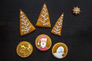 biscoitos de gengibre festivos artesanais em forma de estrelas, flocos de neve, pessoas, meias, funcionários, luvas, árvores de natal, corações para férias de natal e ano novo em fundo preto de madeira foto