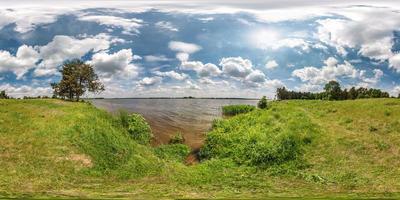 panorama hdri esférico sem costura completo vista de ângulo de 360 graus na costa de grama do enorme lago ou rio em dia ensolarado de verão e tempo ventoso com belas nuvens em projeção equirretangular, conteúdo vr foto