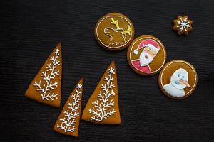 biscoitos de gengibre festivos artesanais em forma de estrelas, flocos de neve, pessoas, meias, funcionários, luvas, árvores de natal, corações para férias de natal e ano novo em fundo preto de madeira foto