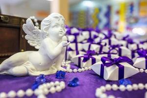 anjo de cerâmica na mesa com uma toalha de mesa violeta e pequenos presentes para convidados dos noivos foto