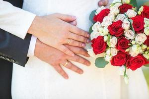 noivo abraça a noiva com buquê de rosa branca vermelha de casamento. anéis nas mãos do casal recém-casado foto