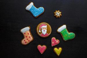 biscoitos de gengibre festivos artesanais em forma de estrelas, flocos de neve, pessoas, meias, funcionários, luvas, árvores de natal, corações para férias de natal e ano novo em fundo preto de madeira foto