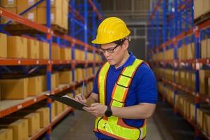 jovem trabalhador usando capacete verificando o estoque e contando o produto na prateleira do armazém moderno. foto