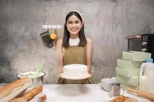 jovem mulher bonita está assando em seu negócio de cozinha, padaria e cafeteria foto