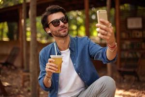 retrato de adorável homem barbudo em óculos de sol posando em lugar público ao ar livre, olhando para a câmera foto