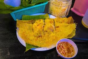 crepes vietnamitas banh xeo recheados com carne de porco ou frango também, camarão, cebola e broto de feijão e molho picante colocado perto do prato na mesa foto