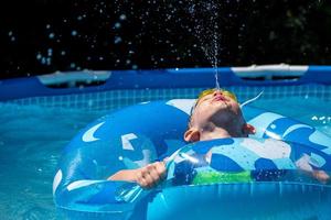 menino cuspindo água para cima na piscina do quintal