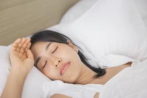 jovem mulher asiática dormindo na cama no quarto. ela está deitada de lado e relaxa com os olhos fechados foto