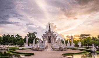 'o templo branco' em chiang rai, também conhecido como 'wat rong khun' em tailandês, a ideia bizarra do artista nacional tailandês chalermchai kositpipat ao pôr do sol. foto
