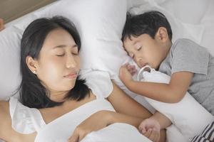 jovem mulher asiática e filho dormindo na cama e relaxando no quarto. eles estão deitados de lado e relaxam com os olhos fechados foto