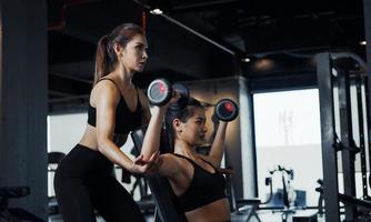 garota esportiva fazendo exercícios de peso com a ajuda de seu personal trainer na academia. foto