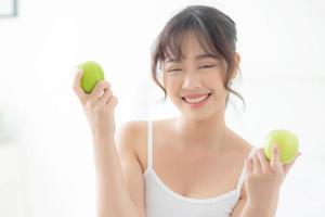 belo retrato jovem mulher asiática segurando e comendo fruta maçã verde no quarto em casa, estilo de vida de nutrição menina saudável e cuidados com o conceito de perda de peso, saúde e bem-estar. foto