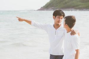 retrato homossexual jovem casal asiático em pé apontando algo juntos na praia no verão, ásia gay indo mar para lazer com romântico e feliz em férias no mar, lgbt com conceito legal. foto