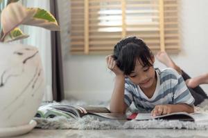 criança lendo livro em casa. menina deitada e lendo dentro de casa foto