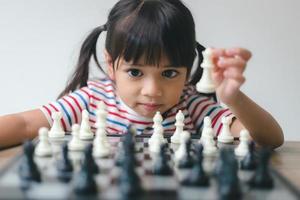 menina asiática jogando xadrez em casa. um jogo de xadrez foto