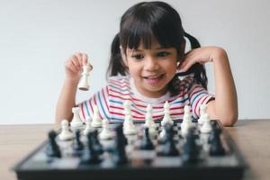 menina asiática jogando xadrez em casa. um jogo de xadrez foto