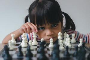 menina asiática jogando xadrez em casa. um jogo de xadrez foto