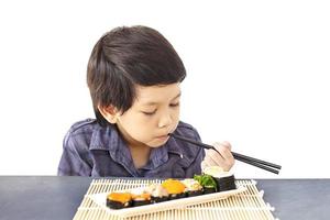 menino adorável asiático está comendo sushi isolado sobre fundo branco foto