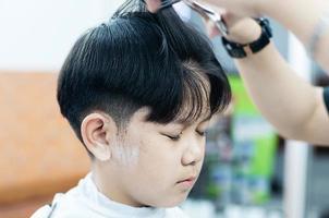 menino asiático é cortado o cabelo na barbearia - pessoas no conceito de salão de beleza de cabeleireiro foto