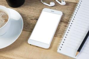 telefone inteligente de tela em branco no trabalho de mesa de madeira. foto