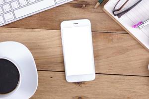 vista superior do telefone inteligente de tela em branco no trabalho de mesa de madeira. foto