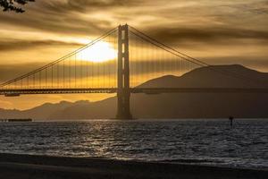 pôr do sol da ponte golden gate e nuvens amarelas douradas ao fundo e a baía de são francisco em primeiro plano foto