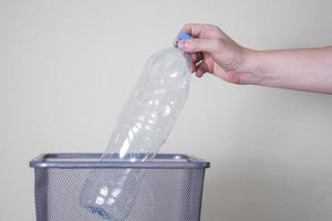 jogue uma garrafa de plástico no lixo em um fundo cinza.