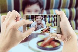 pai tira foto móvel de menino asiático comendo batatas fritas alegremente - criança com conceito de junk food insalubre