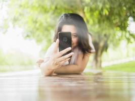 mulher deitada no terraço de madeira tirando foto usando o celular no parque verde