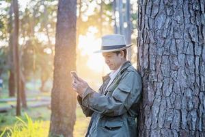 homem asiático com telefone celular na natureza da árvore da floresta - pessoas no conceito de natureza e tecnologia de primavera foto